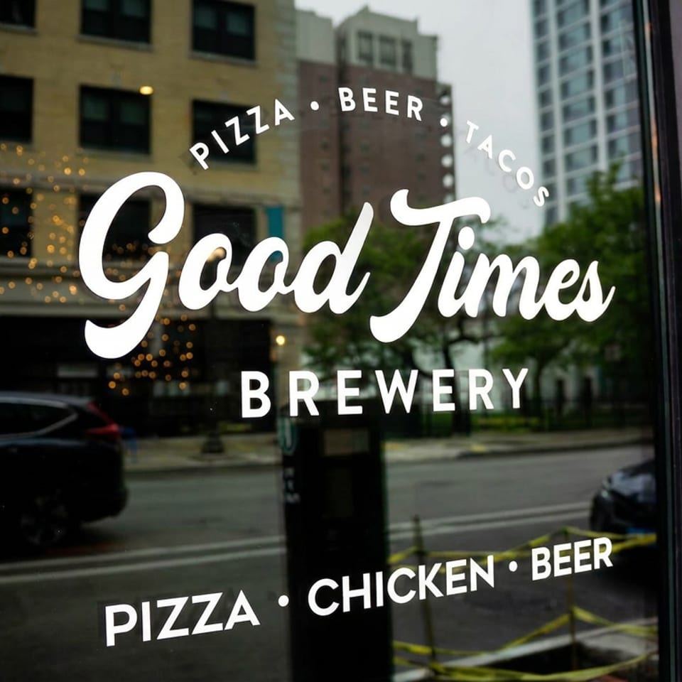 Good Times Brewery storefront window featuring pizza, beer, tacos, and chicken lettering, with hiring notice and QR code.